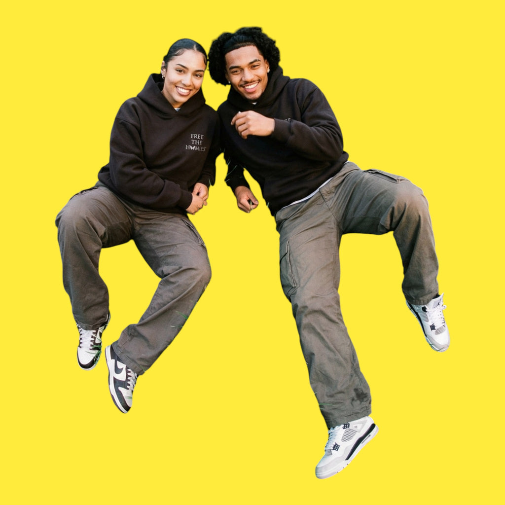Two people in matching Black Out Hoodies by Free The Homies™ against a yellow background
